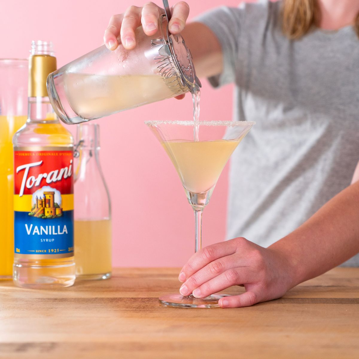torani syrup bottle with a candied lemon drop being poured from shaker into a coupe