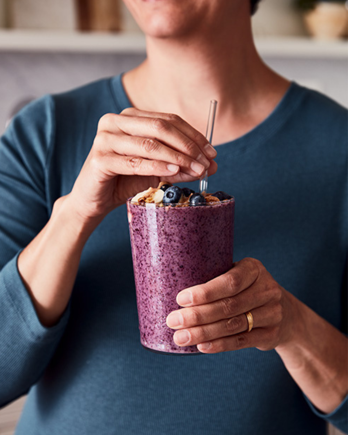 A smiling woman holding a purple fruit smoothie made from blended blueberries and bananas.